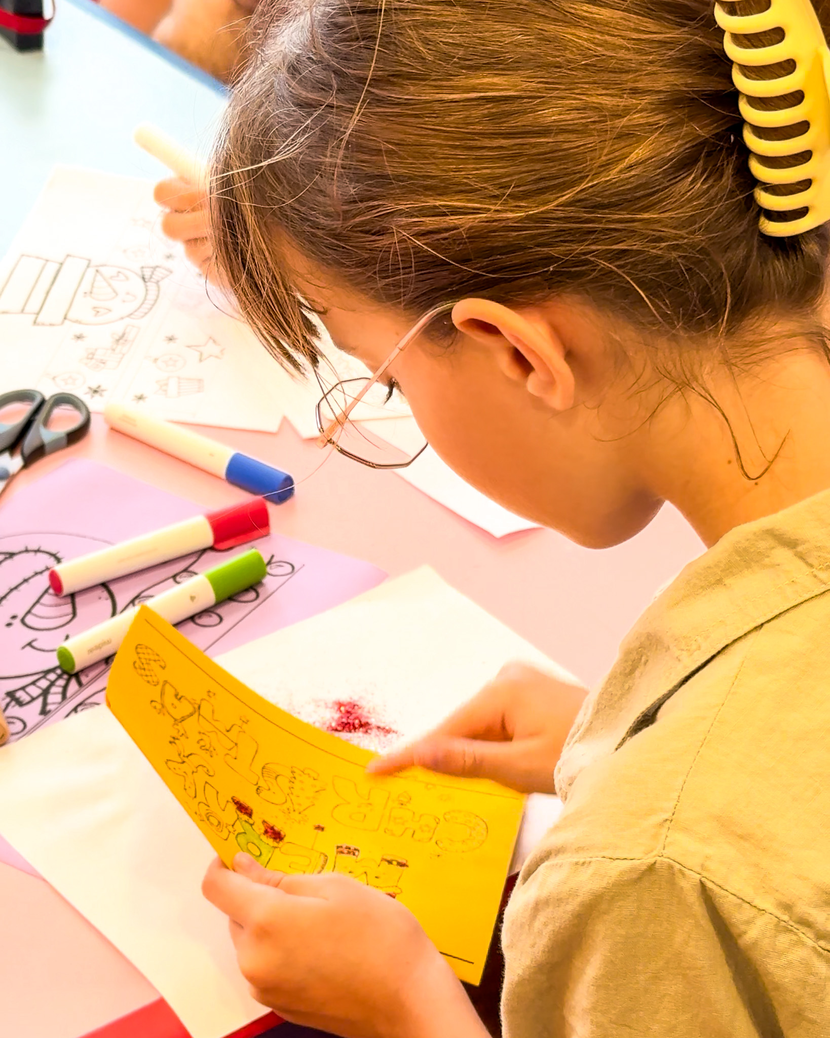 Young girl with a yellow headband doing a Christmas craft activity at a table with colorful markers