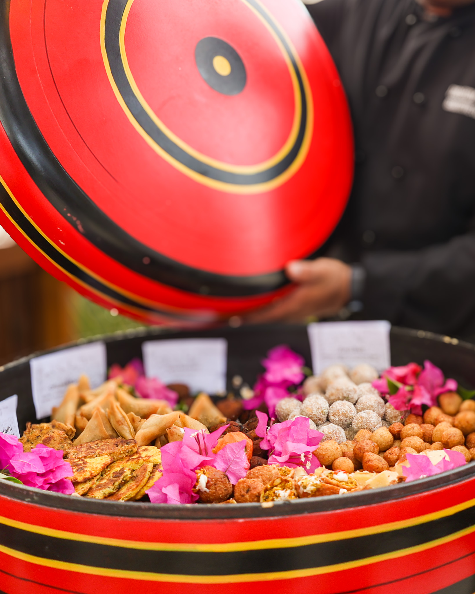 Red and black lacquer container filled with traditional Maldivian snacks and sweets, held by a server