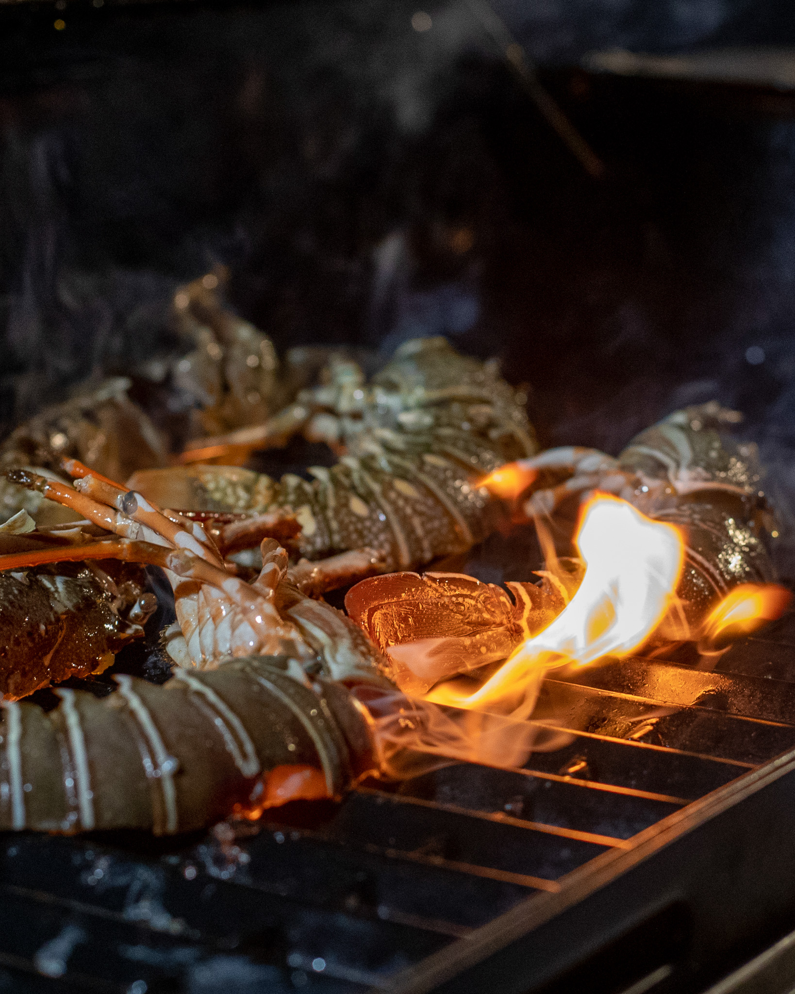 Lobster tails grilling over open flames on a barbecue at night