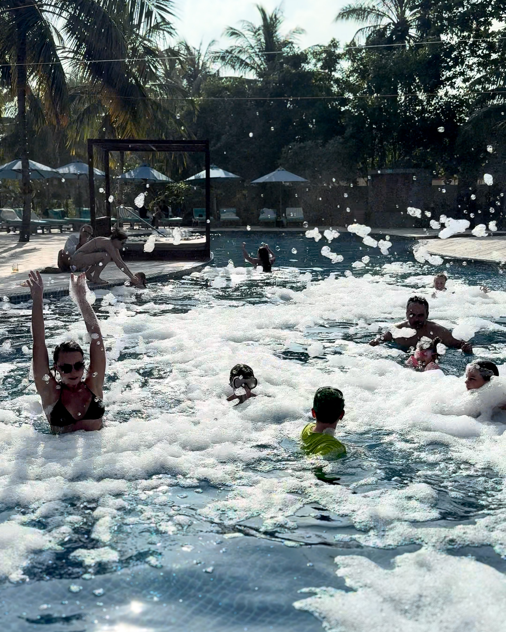 Guests splashing and playing in a sparkling swimming pool with palm trees in the background