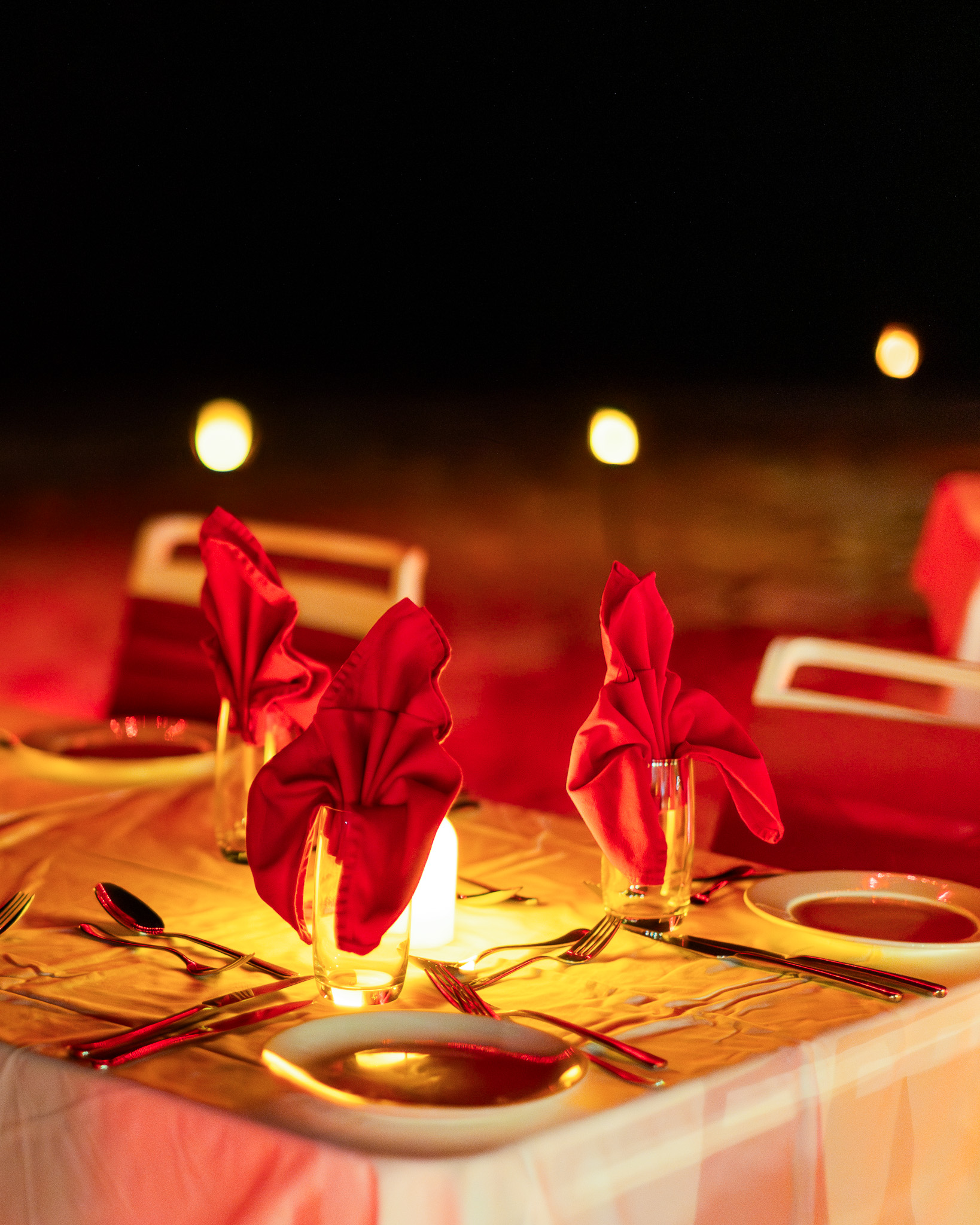 Elegant gala dinner table with red napkins, glowing candles and warm festive lights