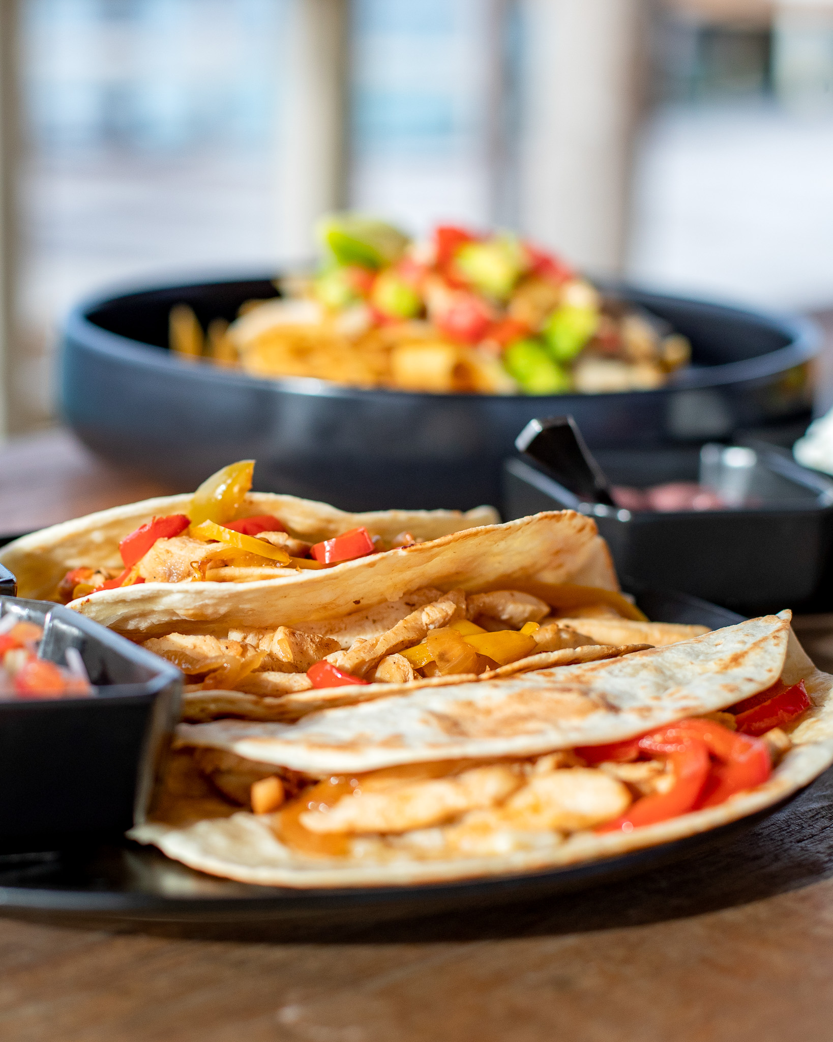Mexican tortilla wraps with grilled fillings served alongside bowls of colorful salad and salsa