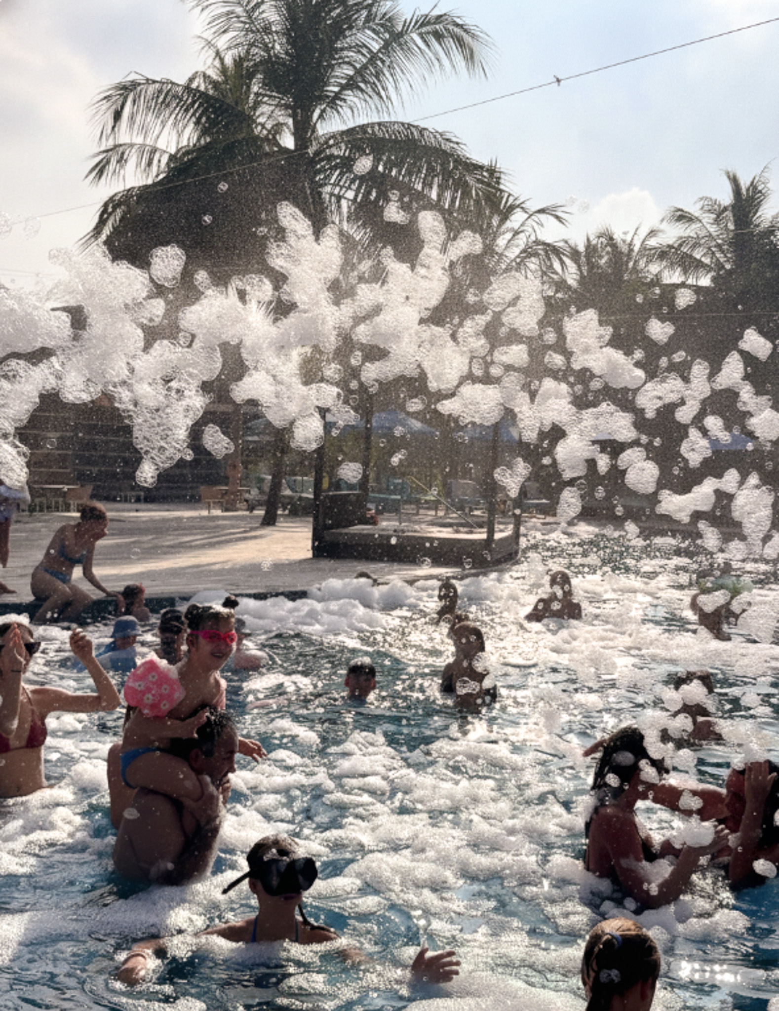 Guests playing a tug-of-war game in a swimming pool with white spray and palm trees in the background